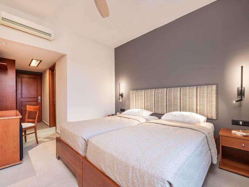 Habitación de hotel moderna con dos camas individuales, lámparas de noche y un escritorio al fondo.