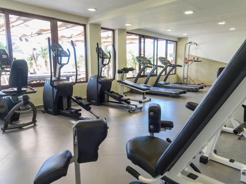 Gimnasio luminoso con equipos modernos y grandes ventanas con vista al exterior.