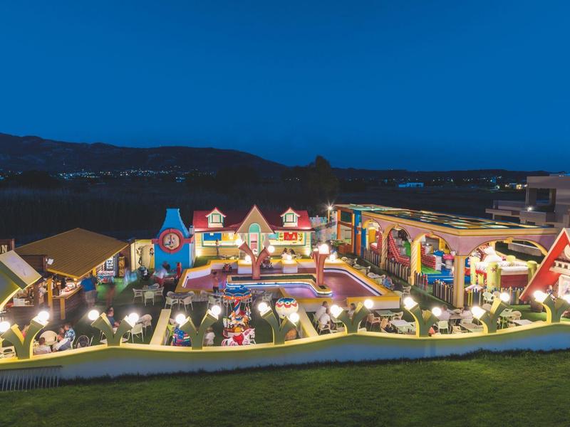 Vista nocturna de un colorido pueblo en miniatura iluminado en el jardín de un hotel.