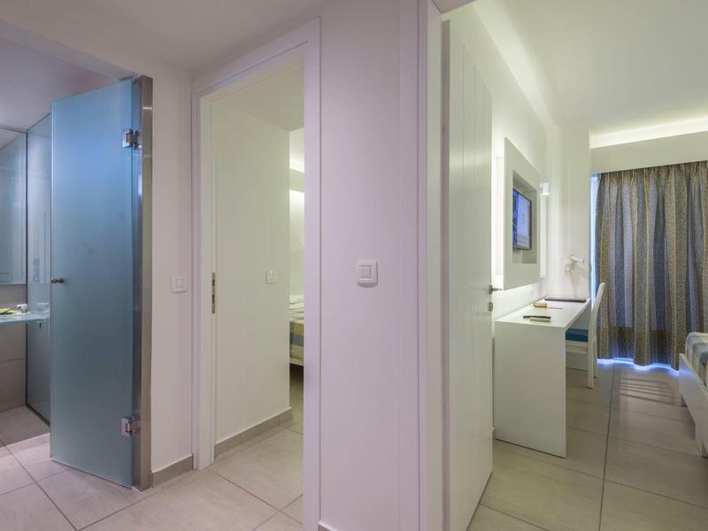 Pasillo moderno de habitación de hotel con baño a la izquierda y zona de dormir al fondo.