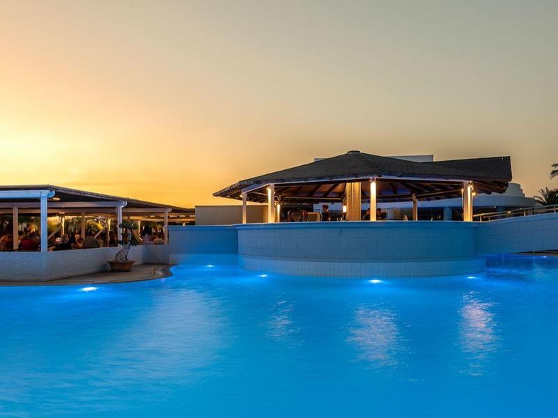Piscina iluminada del hotel al atardecer con agua azul clara y palmeras al fondo