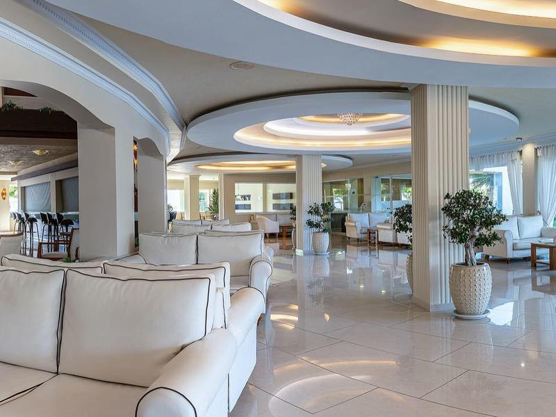 Área de lounge del hotel brillante y moderna con sofás blancos y grandes ventanas con vistas a la naturaleza.