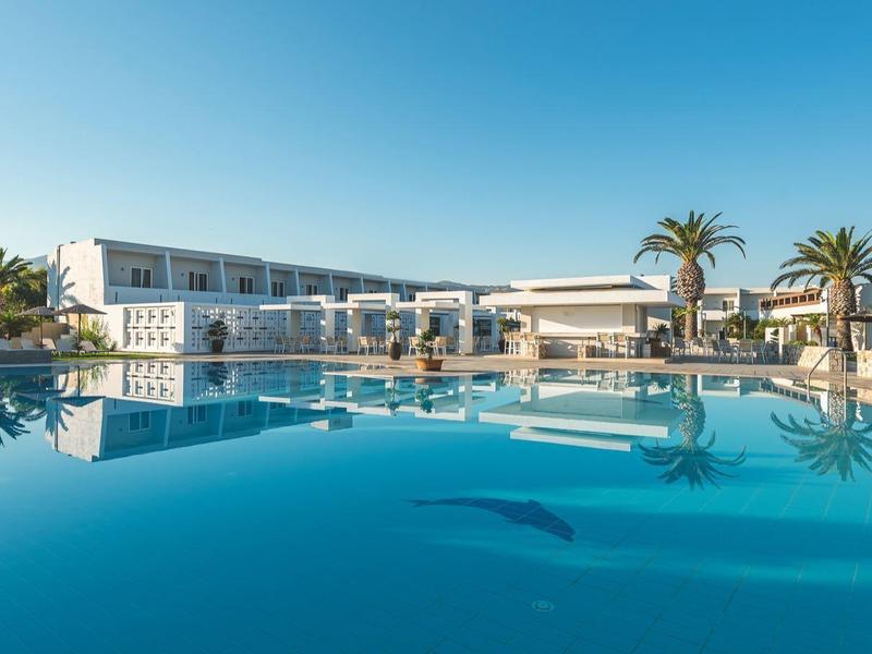 Piscina moderna de hotel bajo cielo despejado con sombrillas y palmeras al fondo.