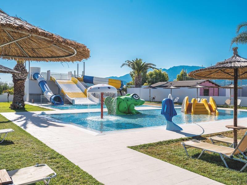 Zona infantil con toboganes acuáticos y sombrillas en la piscina del hotel bajo cielo despejado.