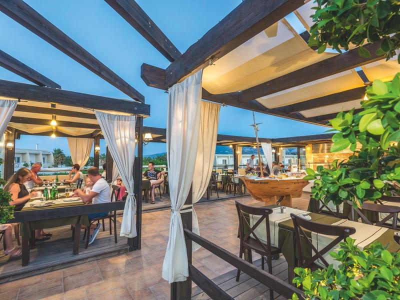 Área de comedor al aire libre en un hotel, con estructuras de madera y plantas decorativas.