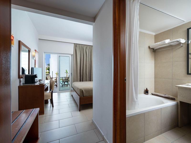 Habitación de hotel moderna con entrada abierta al baño y vista al balcón con vista al mar.