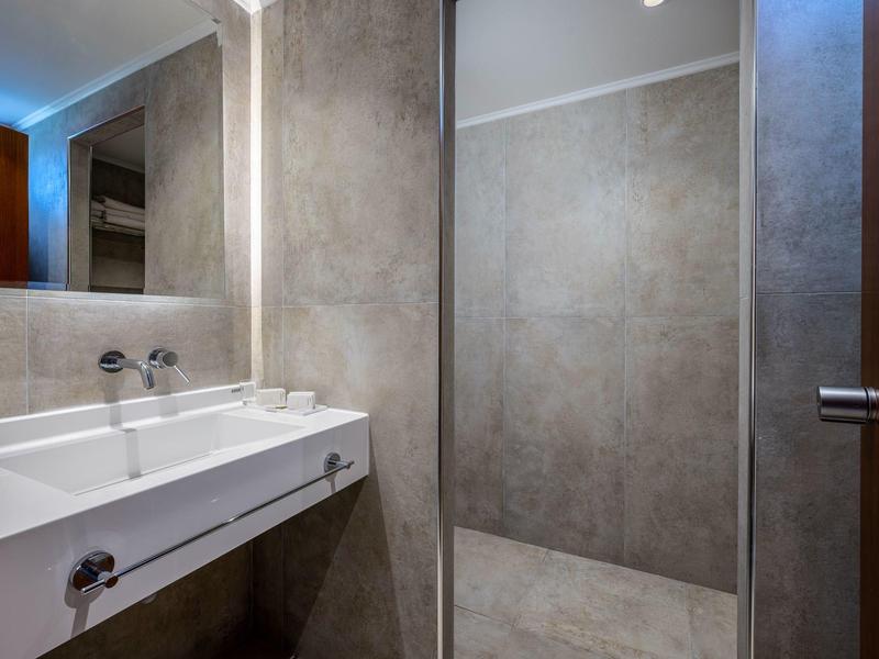 Baño moderno con lavabo doble, espejo grande y paredes de azulejos grises.