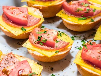 Mehrere kleine herzhafte Muffins mit Ei, Käse, Schinken, Tomaten und grünen Kräutern.