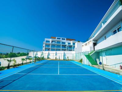 Blauer Tennisplatz vor modernen weißen Gebäuden unter klarem blauem Himmel.