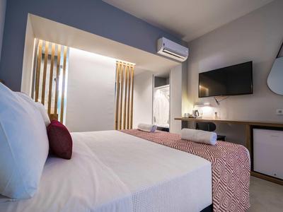 Modernes, helles Schlafzimmer mit großem Bett, weißer Bettwäsche, Fernseher und rundem Wandspiegel.