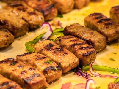 Gegrillte Fleischröllchen mit Röstaromen auf gelbem Teller mit grünen Paprikastreifen und Zwiebelringen.