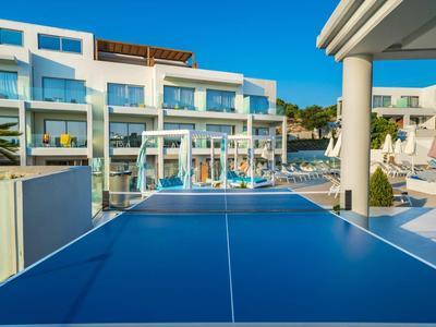 Blauer Tischtennistisch im Freien, dahinter Pool und moderne weiße Hotelgebäude bei klarem Himmel.