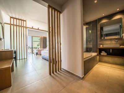 Moderner Hotelzimmerflur mit Holztrennwänden, Badezimmer und Blick ins Schlafzimmer mit hellen Fliesen.