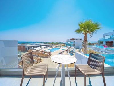 Zwei Stühle und ein runder Tisch auf Balkon mit Pool, Palmen und blauem Himmel im Hintergrund.