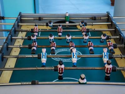 Tischfußballspiel mit rot-weiß gestreiften und blauen Spielfiguren auf grünem Spielfeld.