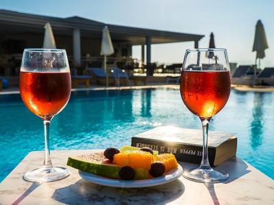 Zwei Gläser Rotwein, Teller mit Früchten und Bücher an einem Pool mit Sonnenschirmen bei Sonnenuntergang.