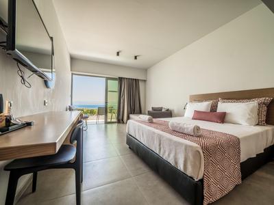 Modernes Hotelzimmer mit Doppelbett, Schreibtisch, Stuhl und Meerblick durch große Fenster.