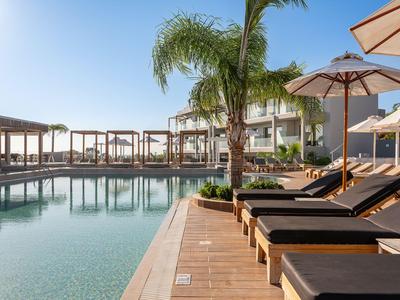 Moderner Hotelpoolbereich mit Sonnenliegen, Sonnenschirmen und Palmen bei klarem Himmel.