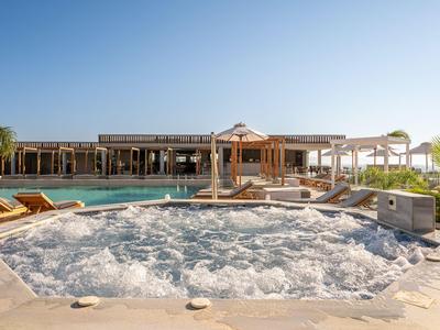 Ein Whirlpool mit sprudelndem Wasser vor einem Resort mit Liegestühlen und einem überdachten Bereich.