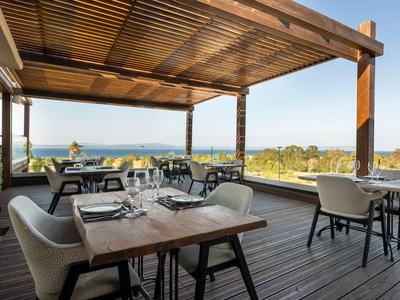 Offene Terrasse mit Tischen und Stühlen, blickt auf das Meer unter blauem Himmel.