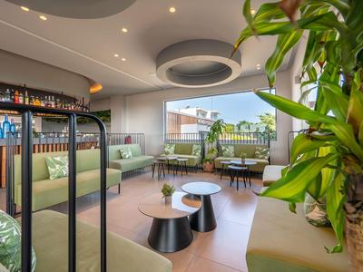 Moderne Hotel-Lounge mit grünen Sitzmöbeln, Tischen und Pflanzen in hellem Raum.