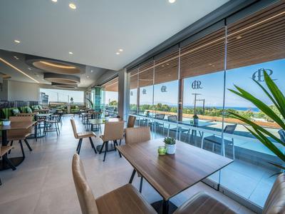 Modernes Hotelrestaurant mit großen Fenstern und Blick auf eine sonnige Terrasse und das Meer.