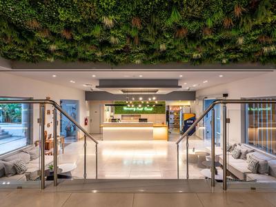 Moderne Hotellobby mit Empfangstresen, Sitzbereichen und grünem Pflanzenwanddekor.