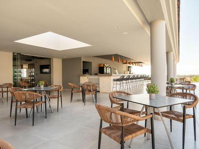 Moderner Außenbereich einer Hotelbar mit Stühlen aus Korbgeflecht und Blick auf grünes Gelände.