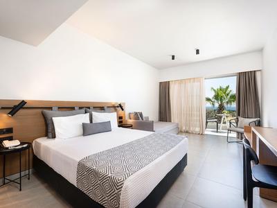 Helles Hotelzimmer mit Doppelbett, Schreibtisch und Balkon mit Blick auf Palmen.