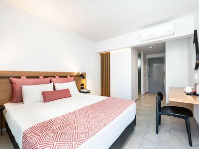 Modernes Hotelzimmer mit großem Bett, Schreibtisch und minimalistischer Einrichtung in neutralen Farben.