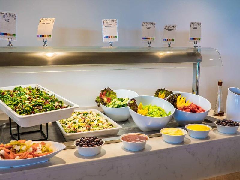 Buffet met saladekommen, dressings en borden op een aanrecht onder warm licht.