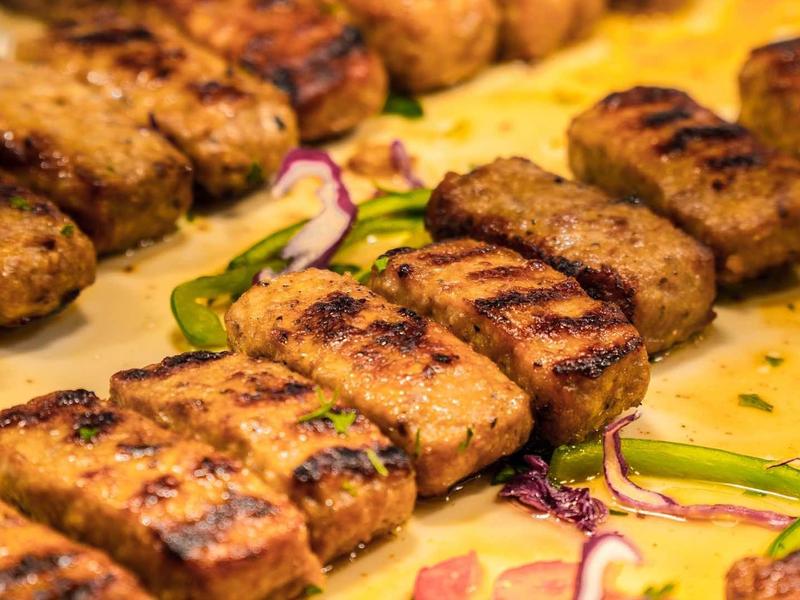 Gegrilde vlees kebabs gerangschikt op een schaal met gesneden groene paprika en ui.