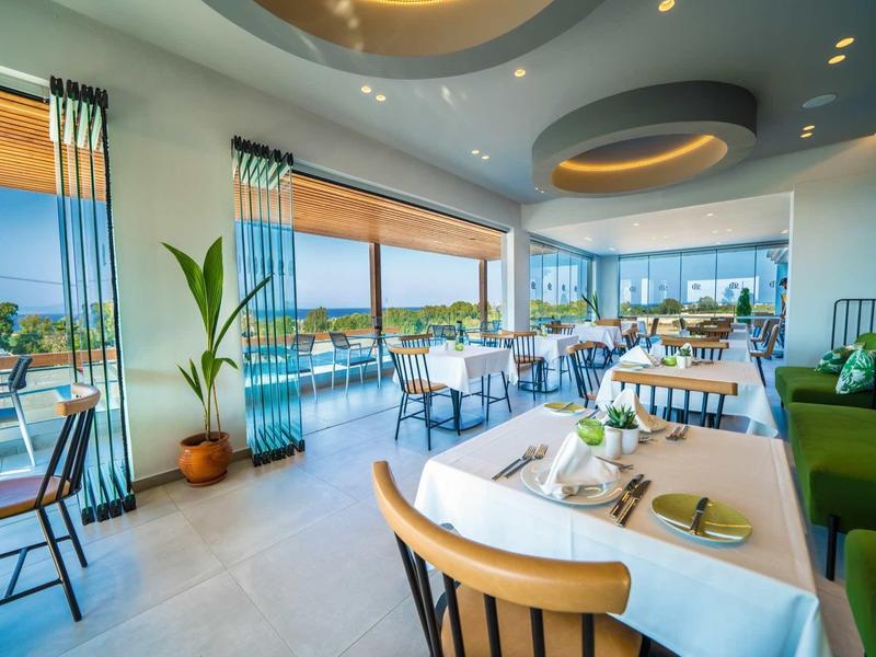 Lichte restaurantinterieur met uitzicht op de oceaan, witte tafelkleden en modern decor.