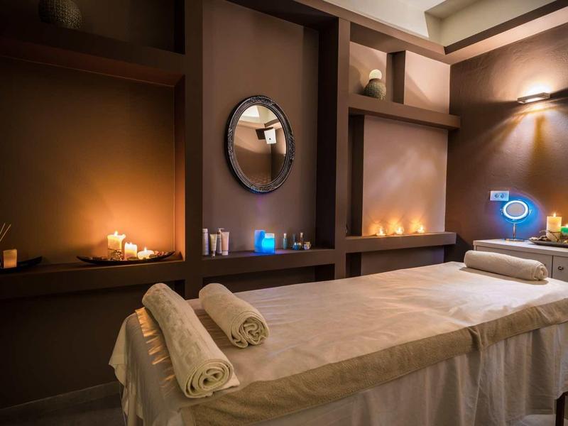 Gezellige spa ruimte met massagetafel, opgerolde handdoeken, kaarsen en zachte sfeerverlichting.