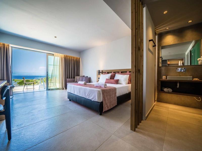 Ruime hotelkamer met tweepersoonsbed, balkon met zeezicht en moderne badkamer.