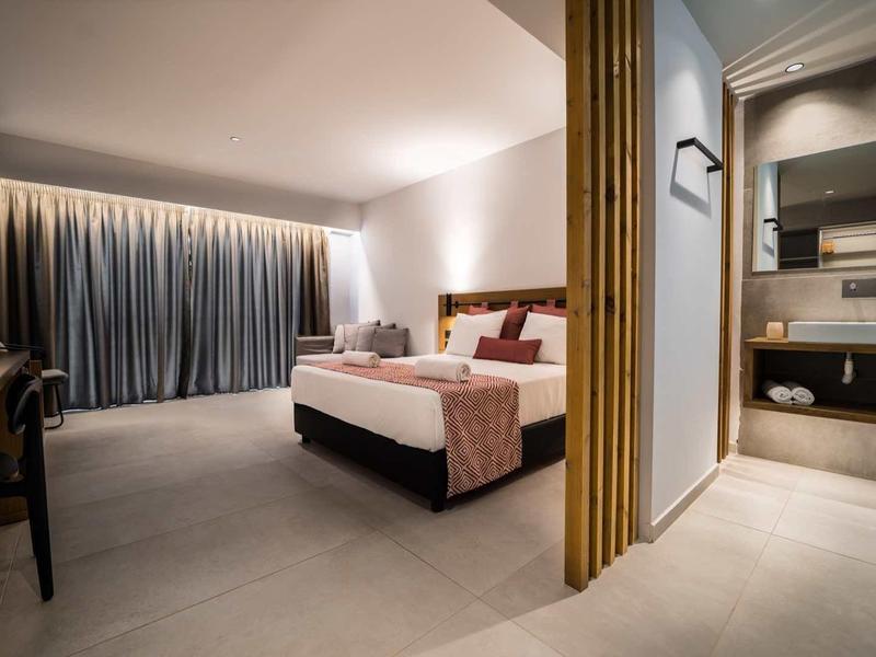 Moderne hotelkamer met groot bed, bureau, gordijnen en aangrenzende badkamer met wastafel en spiegel.