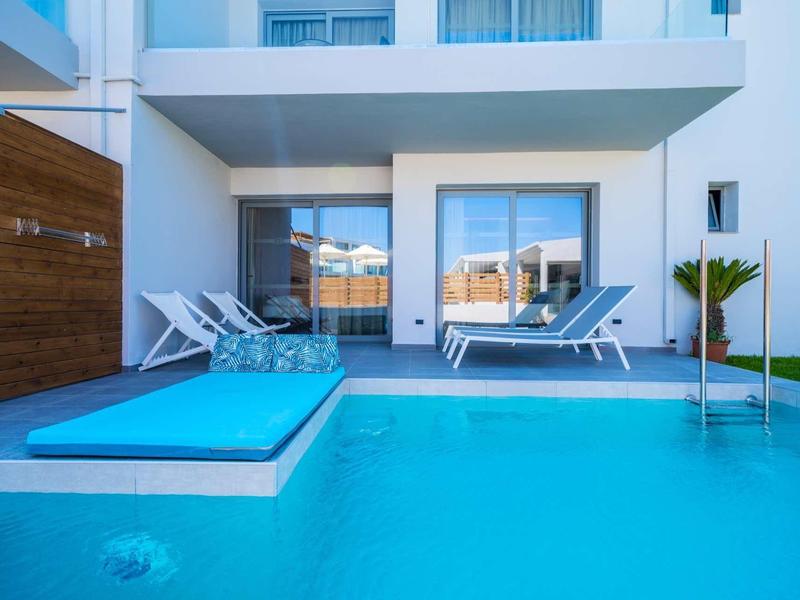 Buitenzwembad met ligstoelen, een blauw kussen en een modern gebouw op de achtergrond.