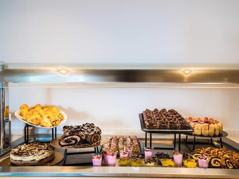 Buffettafel met diverse gebakjes en desserts onder glazen display in hotel.