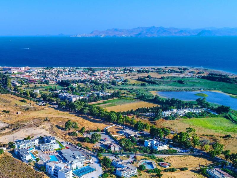 Een kustresort met witte gebouwen, groene velden en blauwe zee onder een heldere hemel.