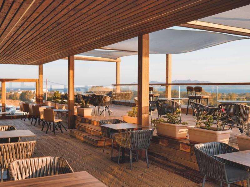 Ruim buitenterras van hotel met houten vloer, dak en zeezicht op de achtergrond.