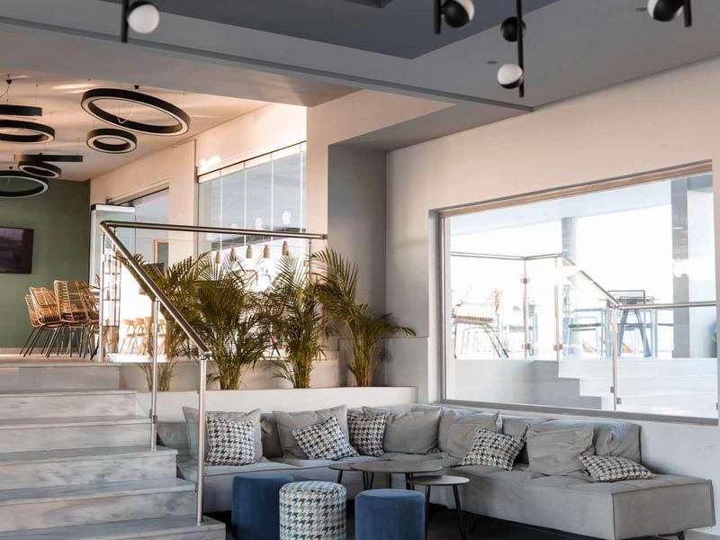 Moderne hotel lobby met grijze hoekbank, verschillende ronde poefs en grote ramen.