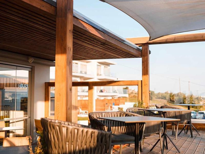 Buiten zitgedeelte met zwarte stoelen en houten vloer onder witte doekluifels.