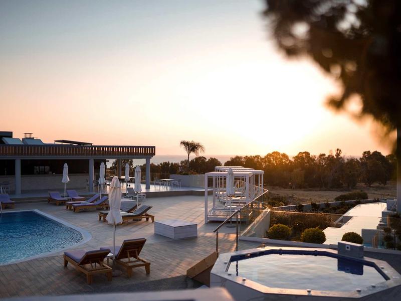 Zonsondergangzicht op een buitenzwembad en jacuzzi omringd door ligstoelen en groen.