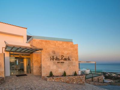 Moderní hotelová budova s kamenným vchodem a výhledem na moře za jasné oblohy.