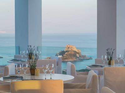 Jasno urządzo­na restauracja z widokiem na morze i skały w oddali.