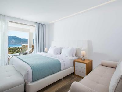 Jasny pokój hotelowy z łóżkiem podwójnym, sofą i balkonem z widokiem na morze.