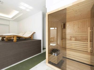 Jasna strefa wellness z drewnianą sauną i dwoma leżakami w spokojnym pomieszczeniu.