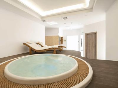Nowoczesna strefa wellness z jacuzzi i leżakami w jasnym pomieszczeniu.