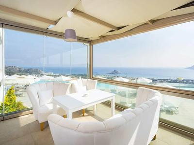 Zastřešený balkon s bílými židlemi a stolem s výhledem na moře.