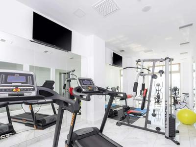 Světle vybavená posilovna s běžeckými pásy, silovým strojem a zrcadlovou stěnou